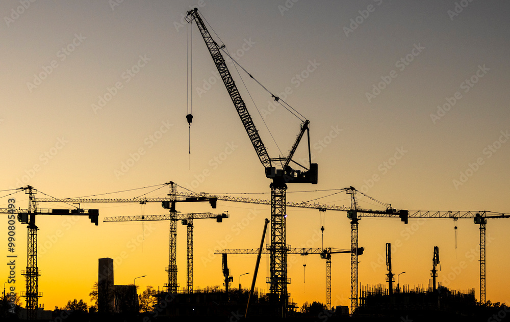 A series of construction cranes rise against a colorful sunset, casting long shadows over a busy construction site, signaling activity in the early evening light. A series of construction cranes rise against a colorful sunset, casting long shadows over a busy construction site, signaling activity in the early evening light.