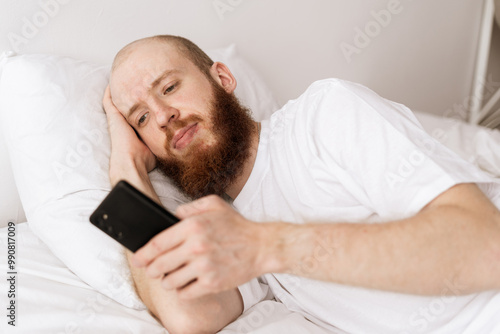 Depression of bearded man using mobile phone relaxing on the bed in bedroom. Tired, mental health and lonely