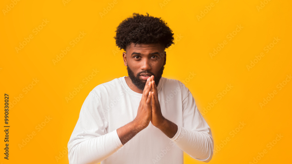 Serious black man holding his hands in praying gesture over orange background Serious black man holding his hands in praying gesture over orange background
