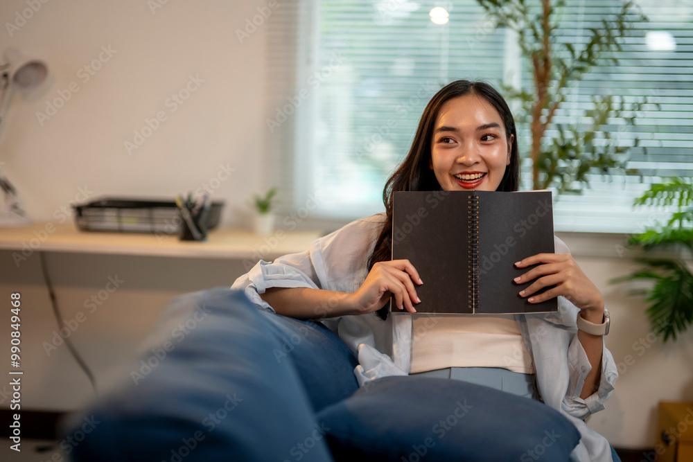 A woman is sitting on a couch holding a black notebook A woman is sitting on a couch holding a black notebook