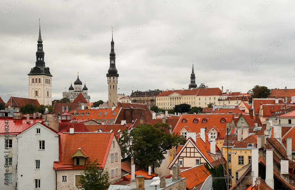 Fototapeta premium The skyline of Tallinn features iconic church towers rising above vibrant rooftops, showcasing the city's rich architecture against a moody overcast sky, reflecting the charm of the old town.