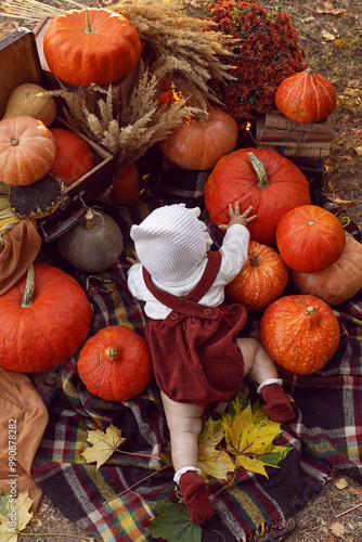 Obraz na płótnie A beautiful baby girl of 8 months in a hat and a suit lies in nature at sunset in the evening with pumpkins around on Halloween w salonie