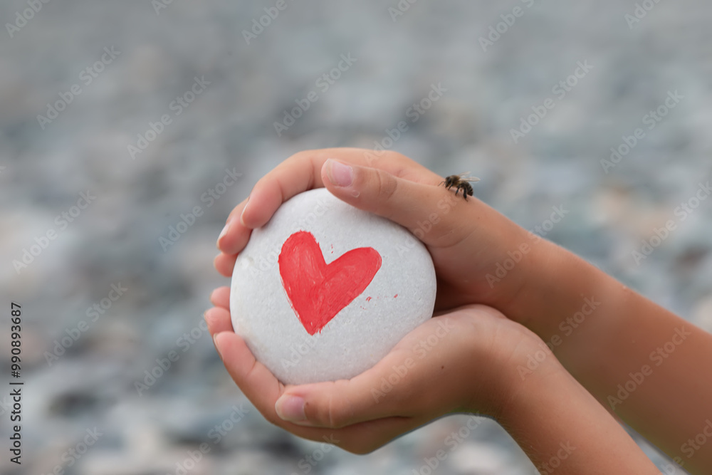 Fototapeta premium The child's hands hold a white stone with a red heart drawn on it.