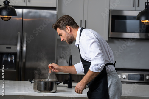 modern chef in professional uniform. close-up on the hand of male chef who is stirring soup in pot with spoon. cooking, culinary and people concept - male chef in toque with pot or saucepan.