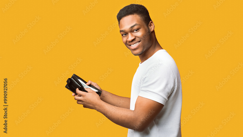 Finance And Investment Concept. Happy afro guy holding wallet full of money, orange wall, panorama, free space Finance And Investment Concept. Happy afro guy holding wallet full of money, orange wall, panorama, free space