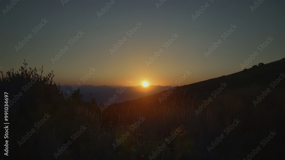 A serene sunset over a mountainous landscape, casting warm hues across the horizon and creating a tranquil atmosphere.