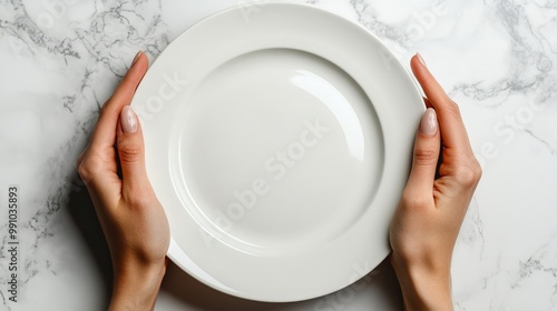 Overhead view of hands holding an empty white plate on a white surface.