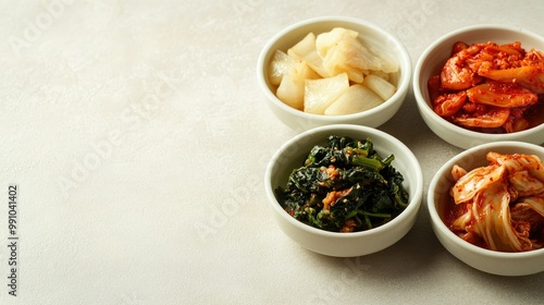 Homemade Korean side dishes including kimchi in small portions, placed on a simple table with ample copy space on a light-colored background.