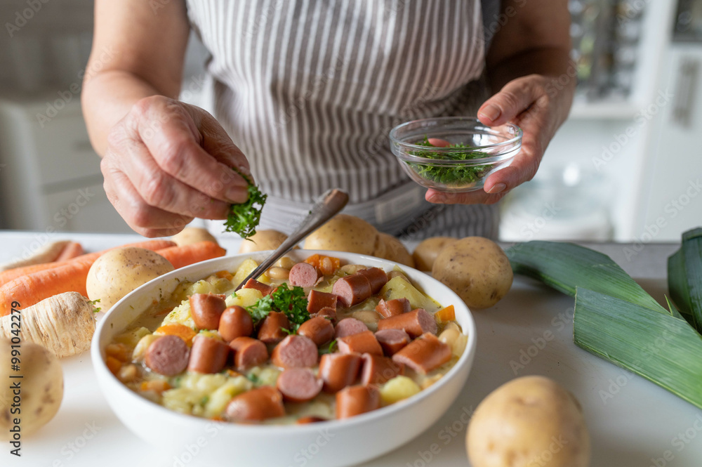 Woman garnishing fresh and homemade cooked potato soup with vienna sausage in the kitchen Woman garnishing fresh and homemade cooked potato soup with vienna sausage in the kitchen