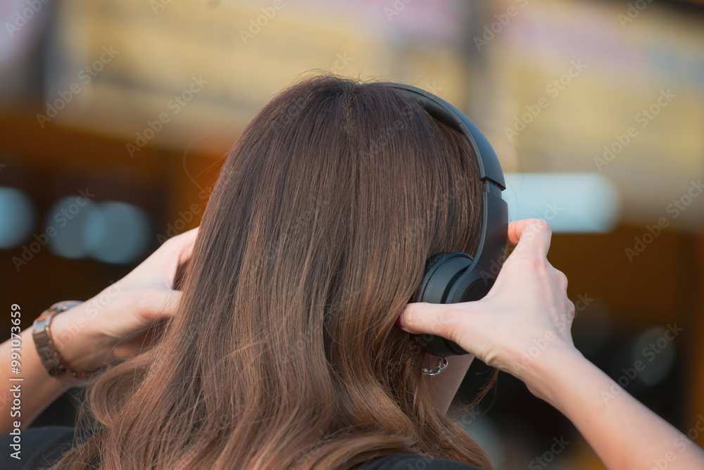Fototapeta premium Young woman wearing black headphones listening to relaxing music after work.