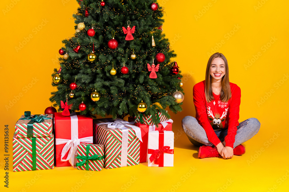 Full size photo of pretty young woman sit floor presents tree wear christmas sweater isolated on yellow color background Full size photo of pretty young woman sit floor presents tree wear christmas sweater isolated on yellow color background
