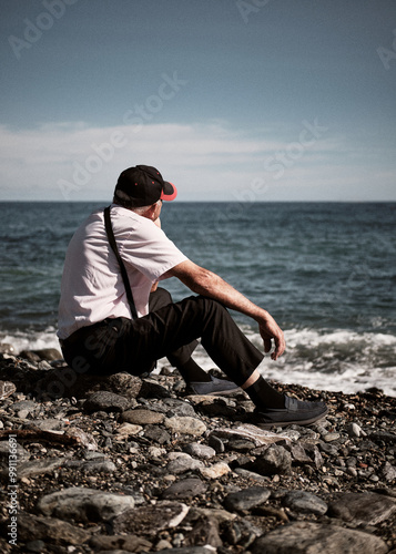 Foto scattata lungo la passeggiata lungomare di Cogoleto ad un uomo seduto in spiaggia mentre osserva il mare. photo