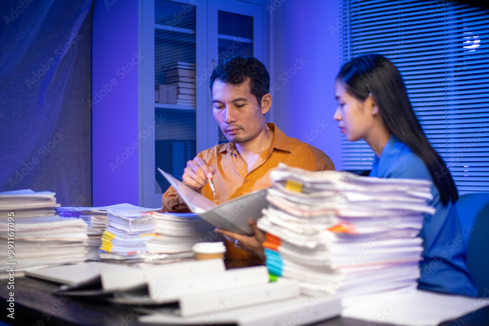 Image of businessman working hard in front of many documents on desk at office late at night with serious action. Concept of working hard and too late. Image of businessman working hard in front of many documents on desk at office late at night with serious action. Concept of working hard and too late.