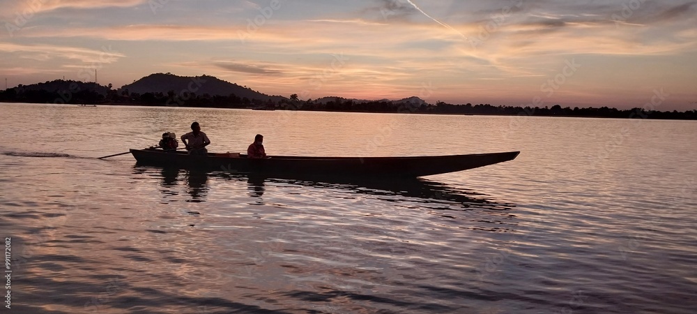 Silhouette of people in a boat during sunset on a calm lake with mountains in the background. Silhouette of people in a boat during sunset on a calm lake with mountains in the background.