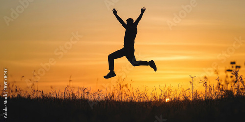 Wallpaper Mural Silhouette of a man mid-jump during a sunset, with arms raised, set against a glowing orange sky and a grassy landscape in the foreground. Torontodigital.ca