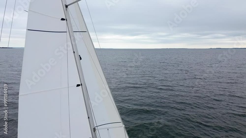  Rear aerial drone 4K film of sailboat yacht sail sailing on sea ocean water into fjord with Dutch holland flag on Baltic sea in Denmark with attached towed dinghy moving away from camera photo