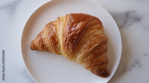 A croissant split open, revealing its soft, airy interior, placed on a white plate against a minimal backdrop, highlighting the texture of the pastry.