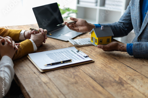 The real estate agent is explaining the terms of the home purchase agreement contract and the client legally signs the contract. Couple is signing a home sales contract with the salesman.