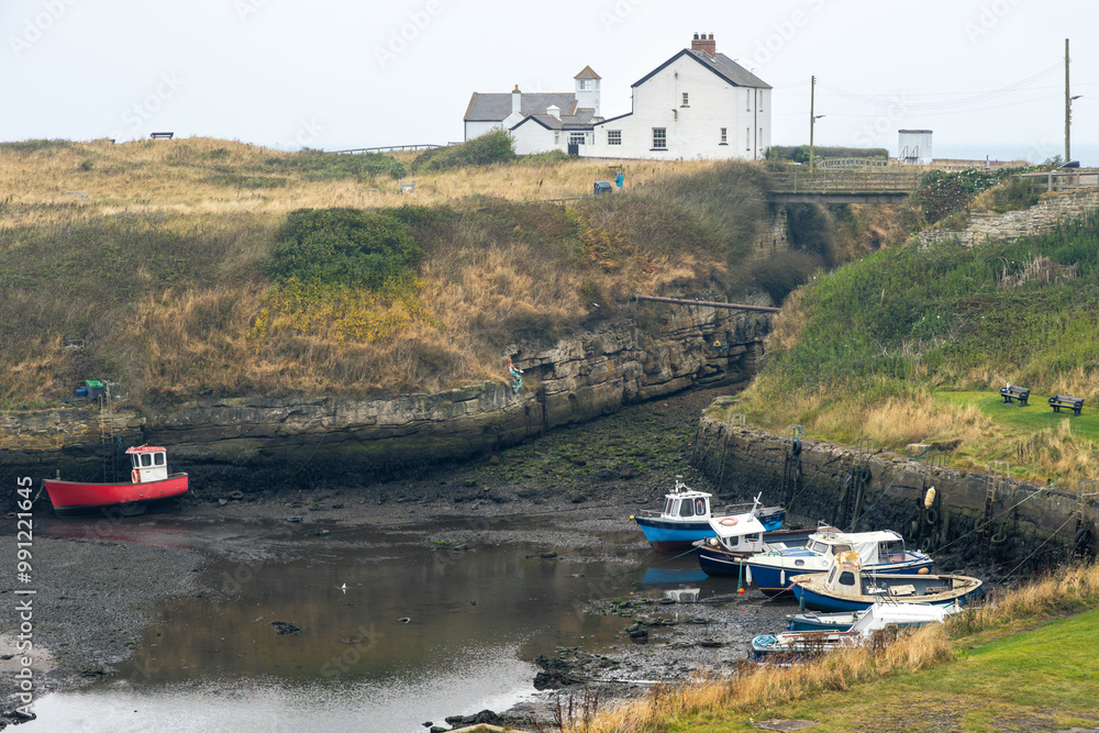 Fototapeta premium Tidal harbour in England with low mud port and small fishing vessel ships run aground waiting for high tide along the beach in grey weather, long exposure image