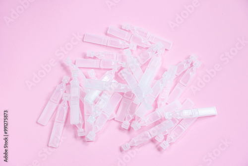 Medical eye drops in plastic pipettes on pink background. Pile of empty plastic ampoules for drops. Plastic vials of saline solution