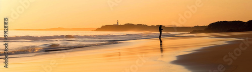 A peaceful beach scene at sunset with gentle waves lapping the shore and a silhouette of a distant lighthouse on the horizon, capturing the beauty of nature and the calm evening atmosphere.