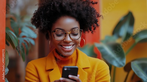 Stylish woman in orange coat using phone on colorful street