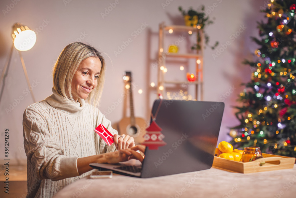Smiling middle aged lady with laptop sitting at home and buying xmas gifts Smiling middle aged lady with laptop sitting at home and buying xmas gifts