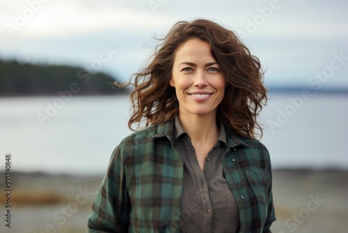 Portrait of a grinning woman in her 40s wearing a comfy flannel shirt while standing against calm bay background photo