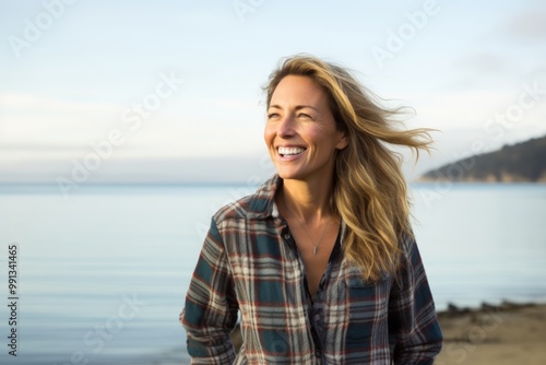 Portrait of a grinning woman in her 40s wearing a comfy flannel shirt in front of calm bay background photo