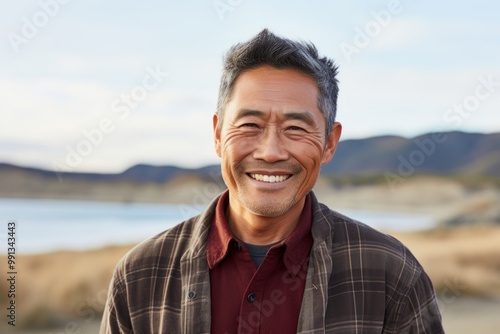 Portrait of a grinning asian man in his 50s wearing a comfy flannel shirt over serene dune landscape background