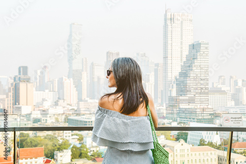 Young pretty woman tourist portrait enjoying Bangkok cityscape skyline panorama. Famous landmark shopping mall over city observation dock. Side view close up bright filter