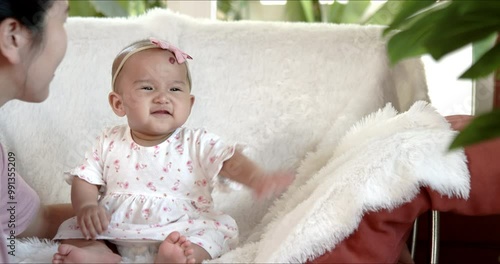 Mom kisses her cute Asian baby girl while playing together at home. Candid shot - Mother and smiling infant laughing and enjoy each other’s company. Happy family fosters joyful and energetic child.
