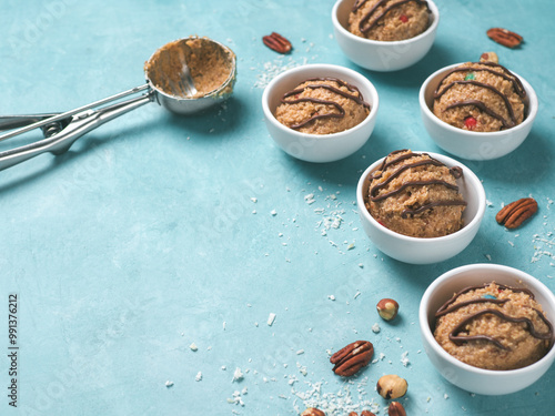 Safe-to-eat raw monster cookie dough in small portion bowl, ice cream scoop and nuts on blue background. Ideas and recipes for kids and toddlers meal. Copy space for text.