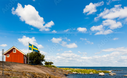 Rotes Schwedenhaus mit Schwedischer Falgge an der Küste am Meer