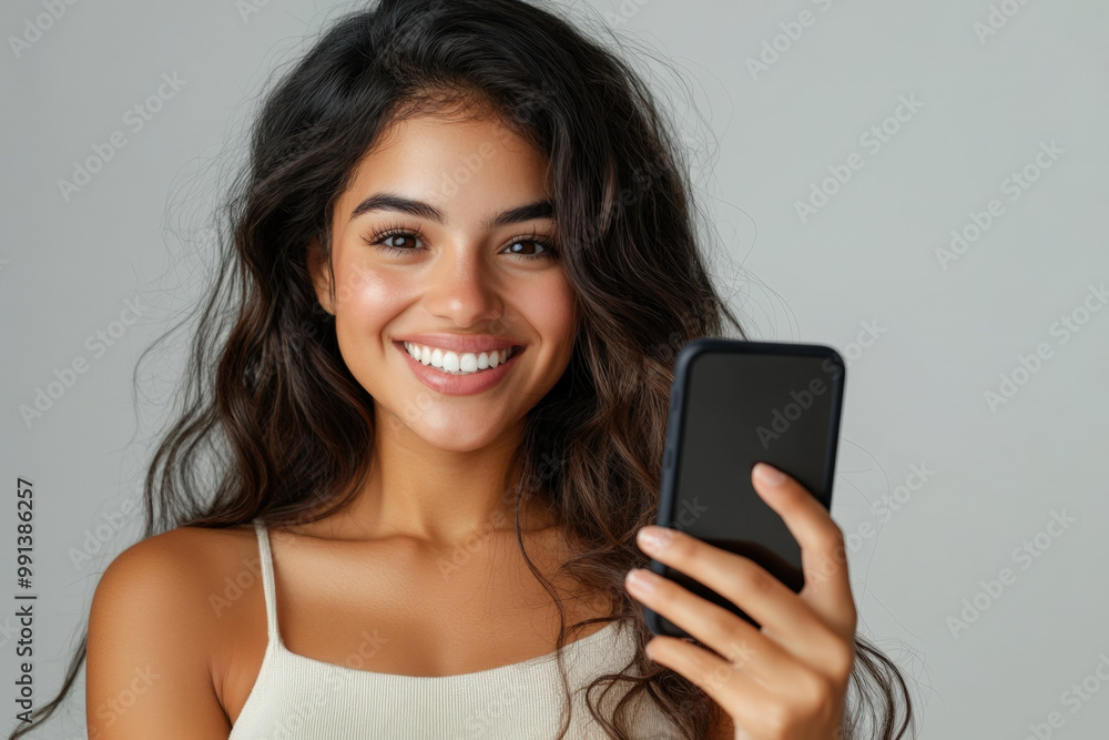 Young woman is holding up her smartphone and smiling after reading something positive on the screen Young woman is holding up her smartphone and smiling after reading something positive on the screen