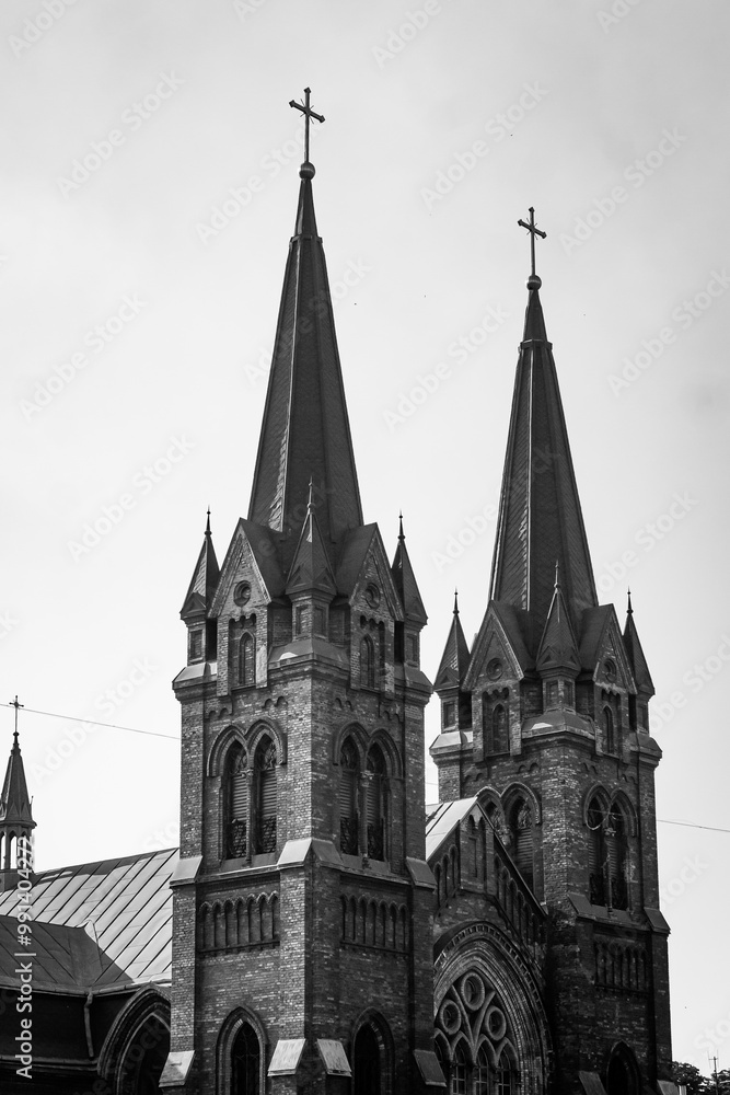 A landscape of urban buildings, Gothic church towers and spires, arched windows of a stone building. Black and white vertical photo from the side of the church facade. A landscape of urban buildings, Gothic church towers and spires, arched windows of a stone building. Black and white vertical photo from the side of the church facade.