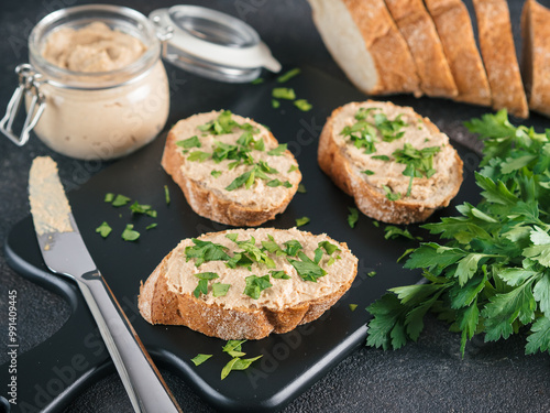 Close up view of slice bread with homemade turkey pate and fresh green parsley on black kutting board over black cement background,