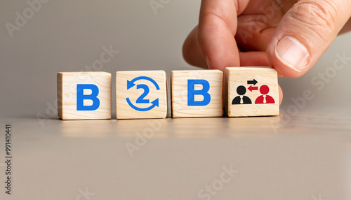 B2B Concept with Wooden Cubes Displaying Business to Business Collaboration, Hand Arranging Cubes with Arrows and People Icons, Symbolizing Partnerships and Exchanges.