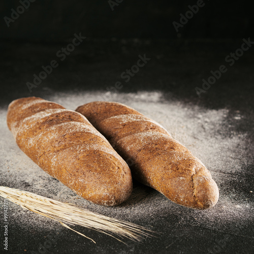 Two whole homemade rye loaf bread with buckwheat flour on black textured background. Copy space. Low key