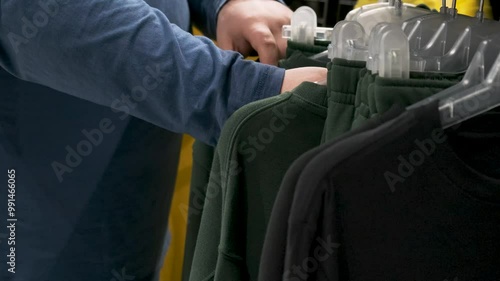 Man choose clothes on hangers in retail store. Male hand browsing clothing on sale, promotion and discount in store. Shopping and retail concept photo