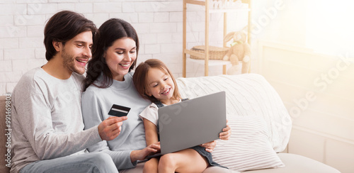 Online Shopping For Family. Happy Parents And Their Little Daughter Using Laptop And Credit Card For Buying Goods In Internet