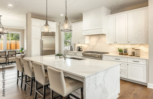 a white kitchen with an island and marble countertop, stainless steel appliances, two bar stools on the left side, and hanging lights above.