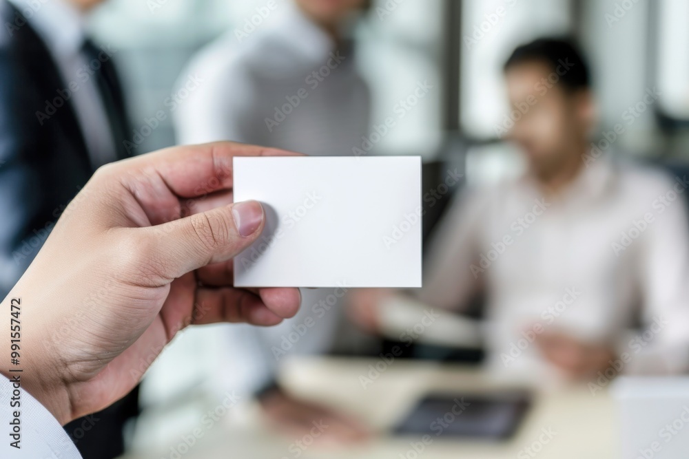 A man holds a white business card in front of a group of people A man holds a white business card in front of a group of people