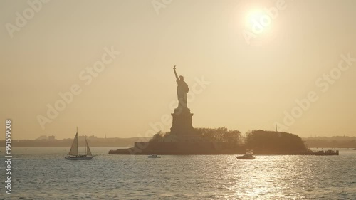 The view of the Status of Liberty and boats from the New York harbor at sunset. New Jersey skyline with Statue of Liberty silhouette on a sunny summer evening. 
