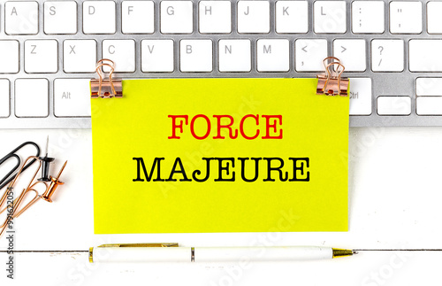 Force majeure text on yellow note with keyboard, paper clips, and pen on white desk photo