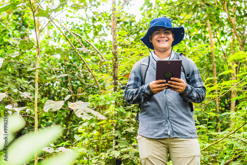 Fotografi A biologist in field clothing smiles at the camera while holding a tablet, using