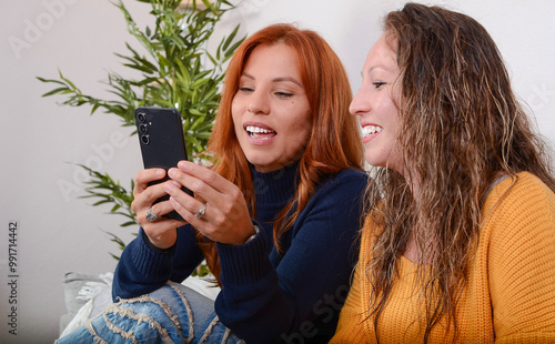 Two sisters showing each other photos on the phone on the couch at home