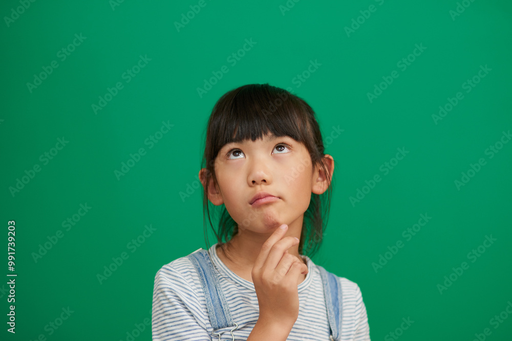 Fototapeta premium Asian child, girl and thinking in studio for future, education or remember by green background. Kid, ideas and problem solving for solution, choice or decision with development, process or memory