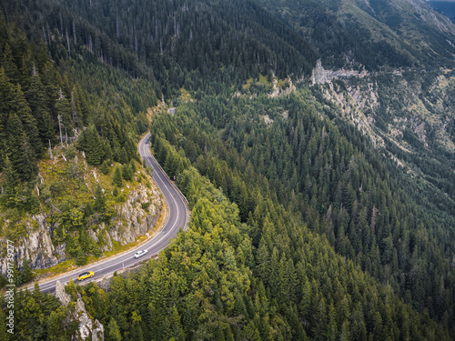 Aerial view of green mountains with a winding road and dramatic cloudy skies above.