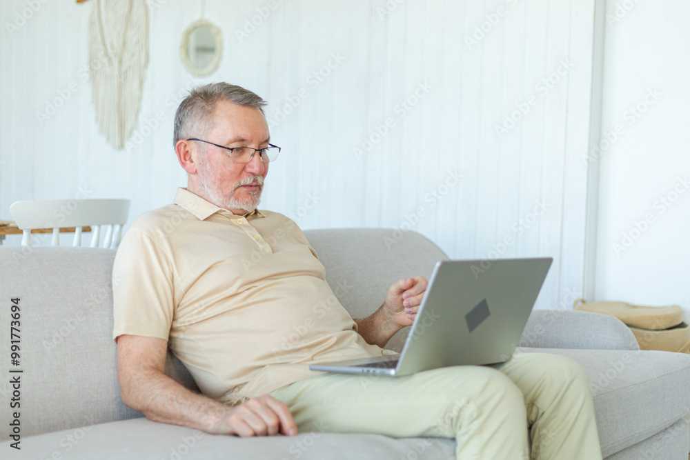 Confident stylish happy middle aged senior man using laptop at home. Stylish older mature 60s beard grandfather sitting at couch looking at computer screen typing chatting reading writing email Confident stylish happy middle aged senior man using laptop at home. Stylish older mature 60s beard grandfather sitting at couch looking at computer screen typing chatting reading writing email